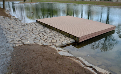Pier for park visitors. two steps lead to it. planks terrace over water. Pond with a dock for...