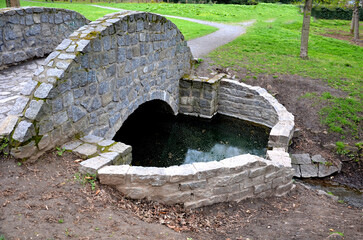 arch bridge, stone granite with railings to the arch. english landscape park. the grassy ditch of...
