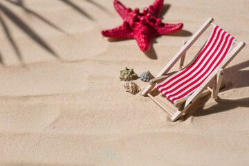 Fototapeta na wymiar A toy beach chaise longue, seashells, a starfish on white sand with shadows. Sunlight. The concept of the sea, a beach holiday and a resort. Summer minimalism.