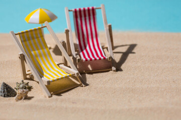 Fototapeta premium A toy beach chaise longue, seashells, a starfish on white sand with shadows. Sunlight. The concept of the sea, a beach holiday and a resort. Summer minimalism.