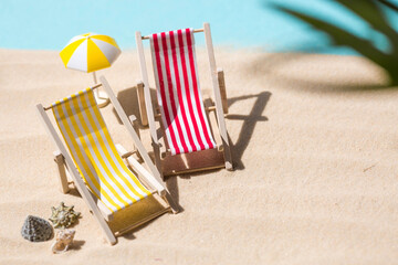 A toy beach chaise longue, seashells, a starfish on white sand with shadows. Sunlight. The concept of the sea, a beach holiday and a resort. Summer minimalism.