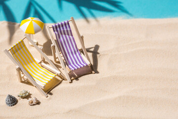 A toy beach chaise longue, seashells, a starfish on white sand with shadows. Sunlight. The concept of the sea, a beach holiday and a resort. Summer minimalism.