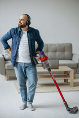 Man doing house work with accumulator vacuum cleaner and listening to music on headphone