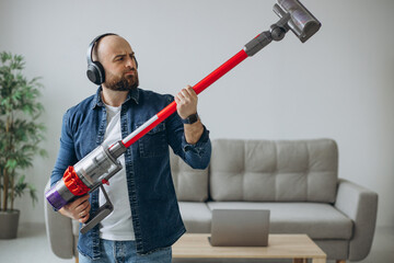 Man doing house work with accumulator vacuum cleaner and listening to music on headphone