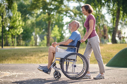 A woman carrying her husband in a wheel chair in a park