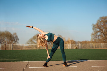 Obraz premium Athletic woman is stretching her arm and side outdoors at the stadium.