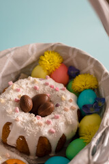 Congratulatory easter card. Easter cake with colored eggs in a white Easter basket. Basket decorated with blue and yellow flowers. Blue hydrangea and yellow chrysanthemum and Easter decor.