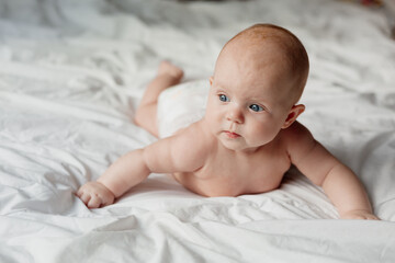 cheerful smiling newborn baby in a diaper lies on his stomach on a white bed