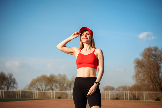 Portrait of smiling caucasian athletic woman in red cap, red top and black cycling shorts outdoors at the sports ground in spring. - Powered by Adobe