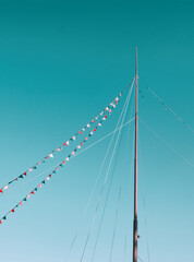 Boat mast draped in colorful flags and pennants on blue sky background. Triangle flag and bunting on ship or yacht lines. Travel and vacation layout, copy space for text. Sea, nautical greetings card.