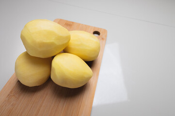 Close-up Several peeled potatoes on a wooden cutting board on a white table.