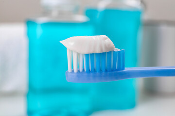Fototapeta na wymiar Toothbrush with paste near mouthwash on blurred background, closeup