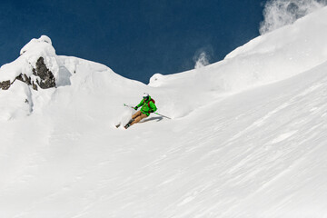 freeride skier energetically rides down on snow-covered mountain slope.