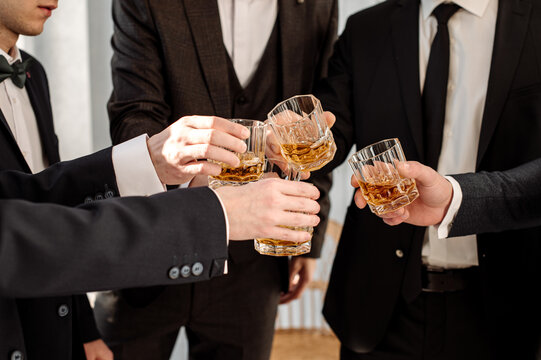 Groom with bestmen drinks whiskey from glasses. Closeup