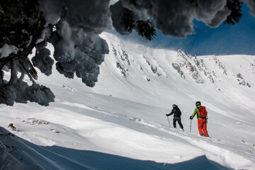 two skiers with backpacks go up the snowy mountain