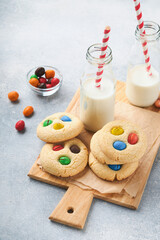 Homemade cookies with colorful chocolate candies and milk. Stack of shortbread cookies with multi colored candy on plate with bottle of milk on light gray background. Baby food concept. Copy space.