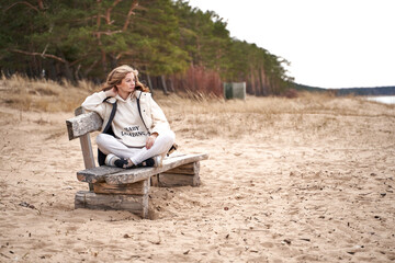 Pregnant woman with text Baby loading on the white hoodie is sitting on the wood bench at the sea shore