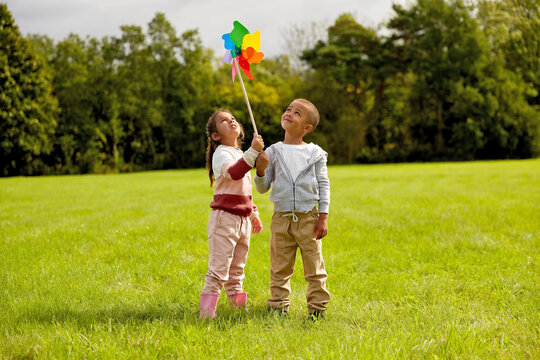 childhood, leisure and people concept - happy little boy and girl playing with pinwheel at park