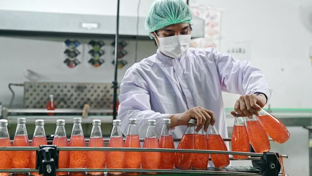 Worker man collecting red juice bottled on conveyor belt in production line at beverage processing factory
