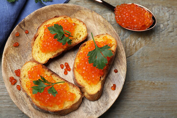 Delicious red caviar sandwiches with parsley on wooden table, flat lay