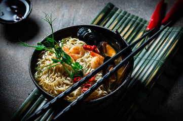 Traditional Japanese soup ramen with shrimp, asian noodles, mussels chili pepper on dark background. Asian style food. Space for text. Noodles with seafood and microgreen