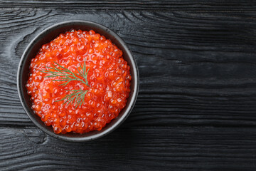 Bowl of delicious red caviar with dill on black wooden table, top view. Space for text