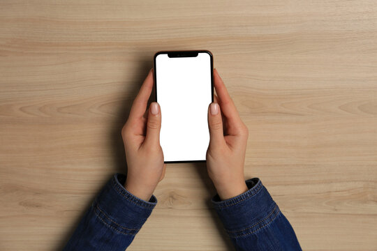 Woman with smartphone at wooden table, top view