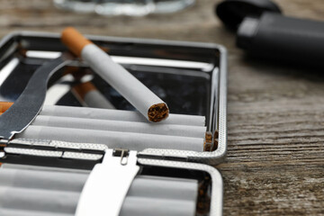 Silver case with tobacco filter cigarettes on wooden table, closeup