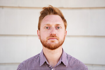 Outdoor portrait of a Red hair guy looking at the camera serious with serene face. Close up of a concentrated man - Caucasian young guy. People and emotions.