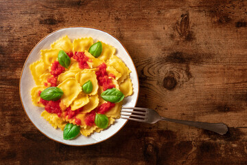 Ravioli with tomato sauce and basil. A plate of stuffed pasta, shot from above on dark rustic wooden background with copy space
