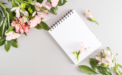 a blank notebook with white sheets on a black spring on a pastel background with spring flowers. top view. a copy of the space.