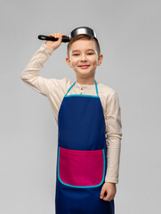 cooking, culinary and profession concept - happy smiling little boy in apron playing with saucepan over grey background