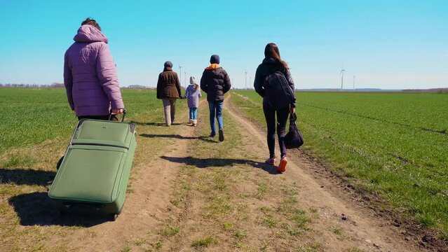 Sad family of ukrainian refugees walking to border with Poland by country road. Concept of peaceful and carefree life without armed conflicts