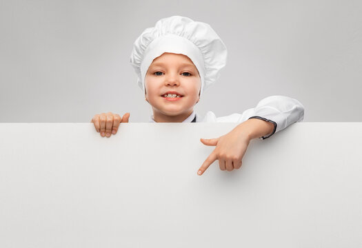 cooking, culinary and profession concept - happy smiling little girl in chef's toque and jacket with white board over grey background