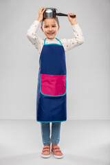 cooking, culinary and profession concept - happy smiling little girl in apron playing with saucepan over grey background