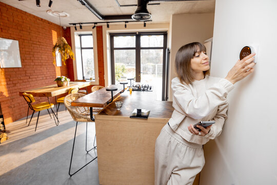 Woman Controlling Home Temperature With Electronic Thermostat Mounted On The Wall In Living Room At Home. Concept Of Modern Technologies And Smart Home