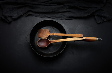 Empty round cast iron frying pan with wooden handle on black table, top view