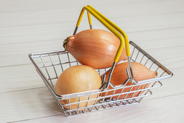 Onions in a metal shopping basket on a background of light wooden boards