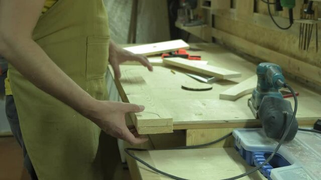 A mature carpenter makes a shelf in his carpentry workshop, works with a tool with wood