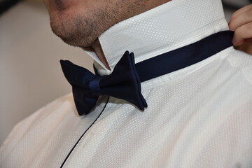 the groom puts on his bow tie on his wedding day