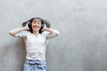 Young excited woman listening to the music in wireless headphones lying relaxed on gray concrete background