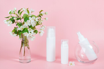 Set of cosmetic for skin care face, body. White blank cosmetics bottles and tube on glass podium and flowering branch in vase, pink background. Natural Organic Spa Cosmetic Beauty Concept Mockup