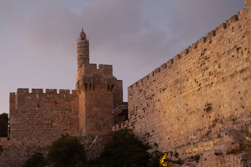 Twilight view of the landmark, stone Tower of David minaret as seen through branches and leaves of trees along the golden sunset walls of the Old City of Jerusalem. © Yehoshua Halevi