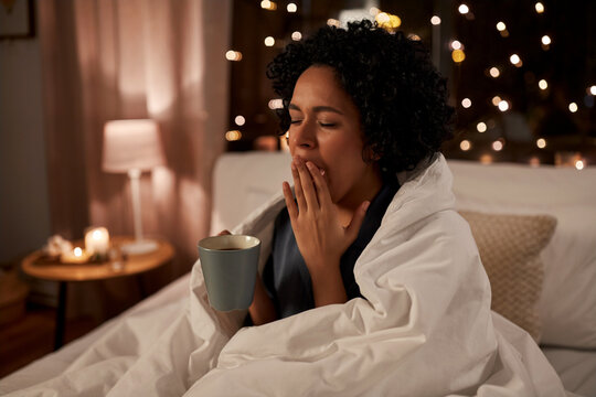 people, bedtime and rest concept - tired sleepy woman in pajamas wrapped in blanket with coffee yawning in bed at night
