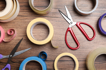 Rolls of adhesive tape and scissors on wooden background, flat lay