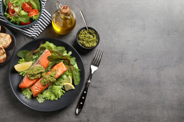 Tasty cooked salmon with pesto sauce served on dark grey table, flat lay. Space for text