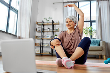 sport, fitness and healthy lifestyle concept - smiling senior woman exercising with laptop computer on mat at home