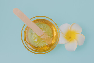 Liquid yellow sugar paste, wooden spatula and flower on a blue background. Removing unwanted hair. Sugaring. Depilation. Epilation. Beauty.  - obrazy, fototapety, plakaty