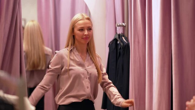 Pretty blonde woman spinning around in front of her boyfriend in new clothes in the fitting room in a clothing store