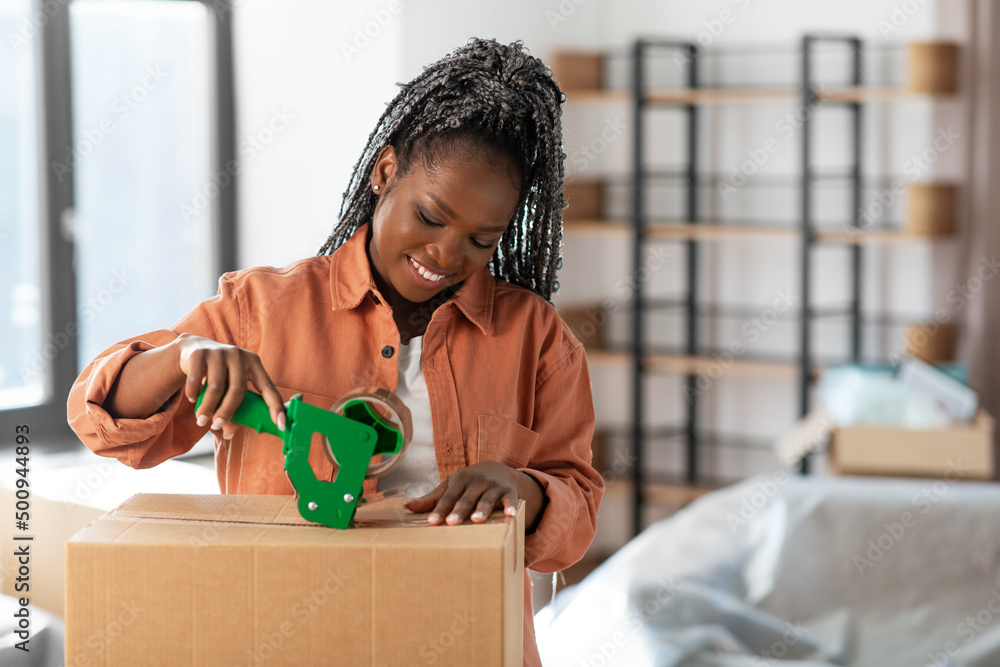 Sticker moving, people and real estate concept - happy smiling woman with adhesive tape packing box at new home